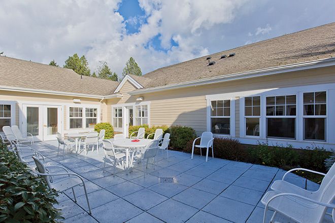 A sunny outdoor patio with white chairs and tables surrounded by a house.