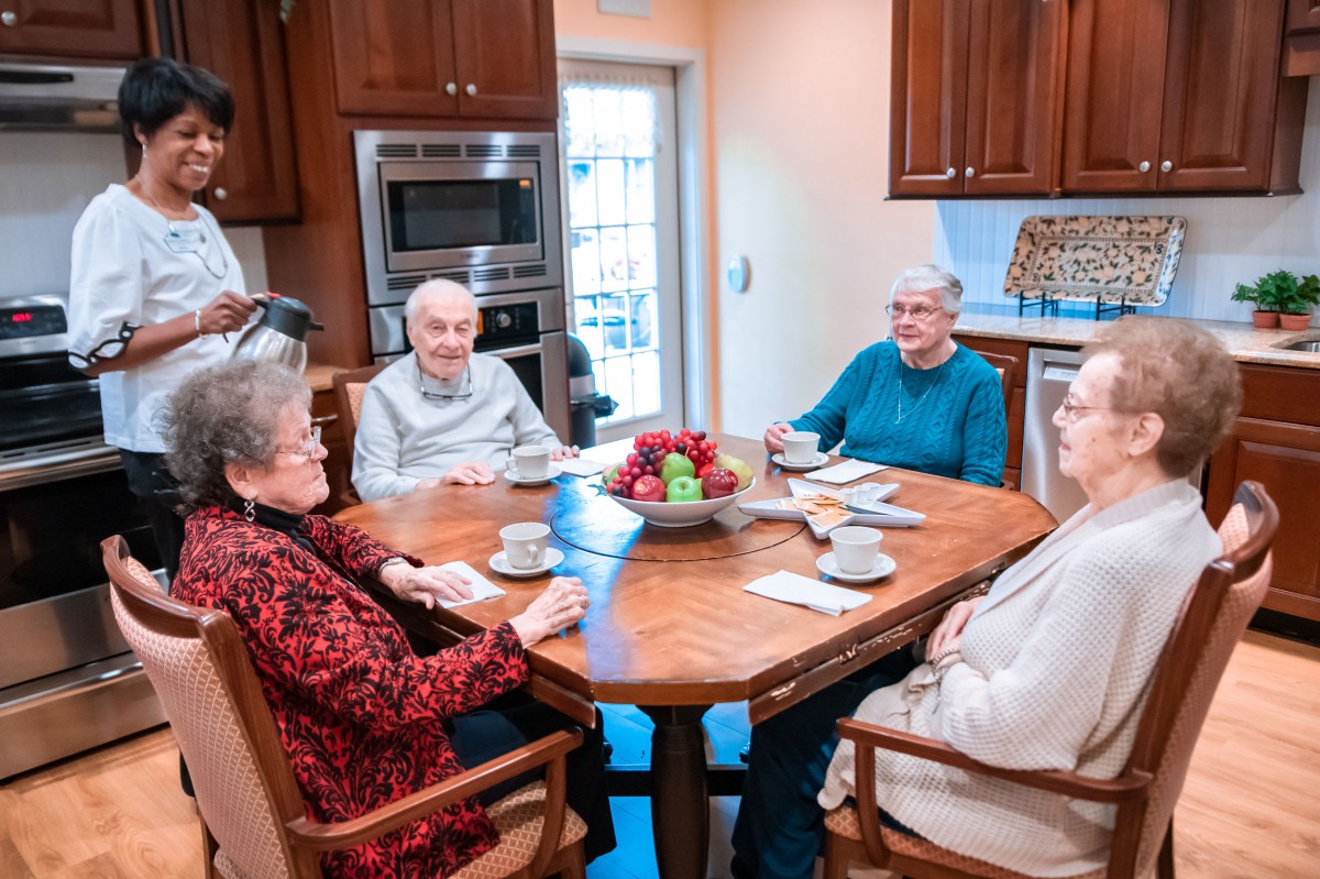 A group of seniors enjoying coffee and conversation around a kitchen table.