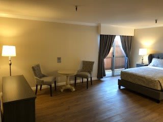 Spacious hotel room with a bed, seating area, and large curtains.
