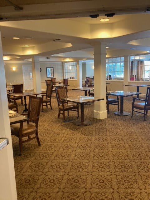 An empty dining room with neatly arranged tables and chairs on a carpeted floor.