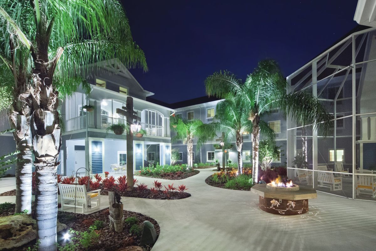 A beautifully lit hotel courtyard at night, featuring palm trees and a cozy fire pit.