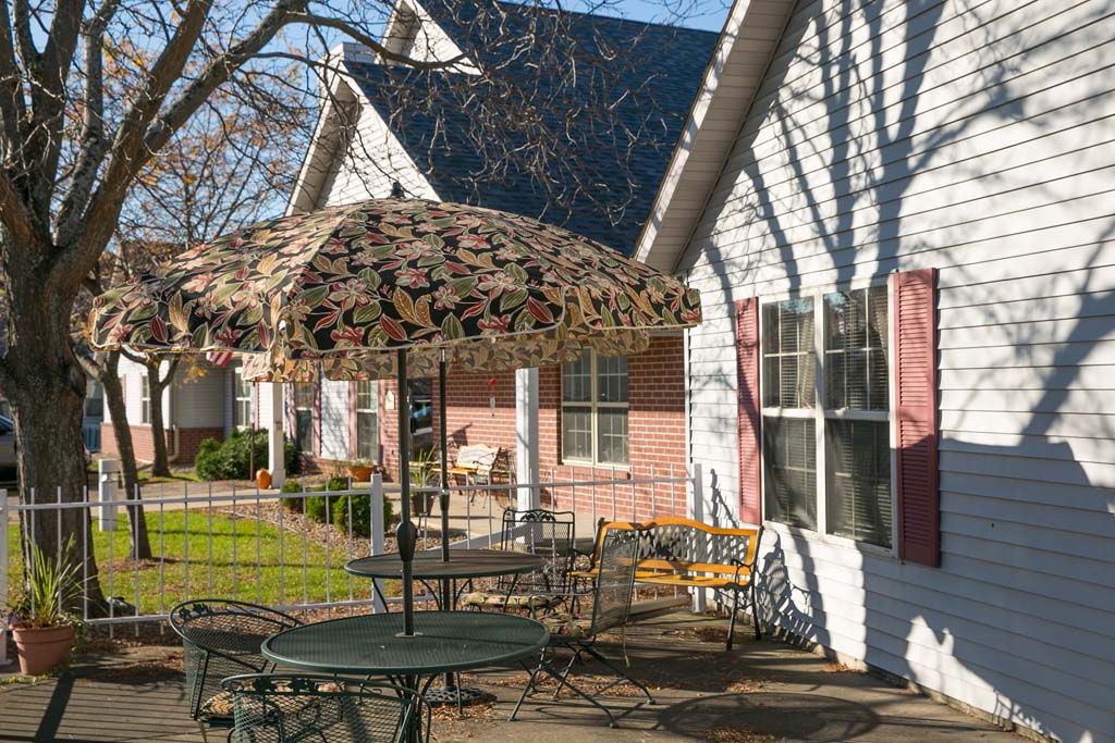 A cozy outdoor patio area with a table, chairs, and an umbrella in front of a house.
