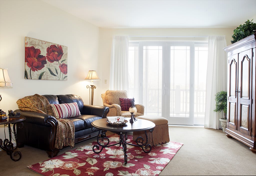 A cozy living room with a sofa, armchair, and coffee table, accented by floral artwork and a rug.