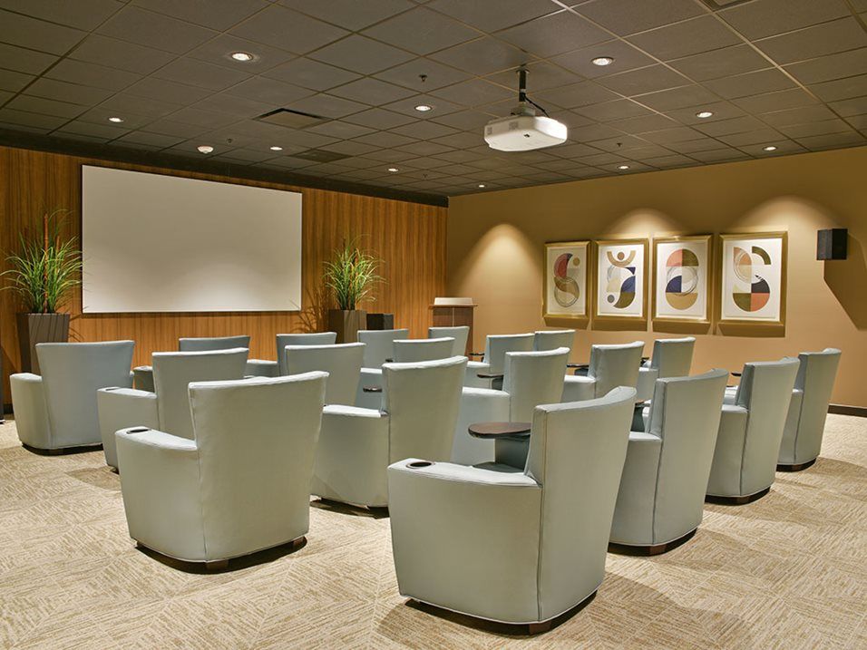 A conference room with theater-style seating and a projector screen, ready for presentations.