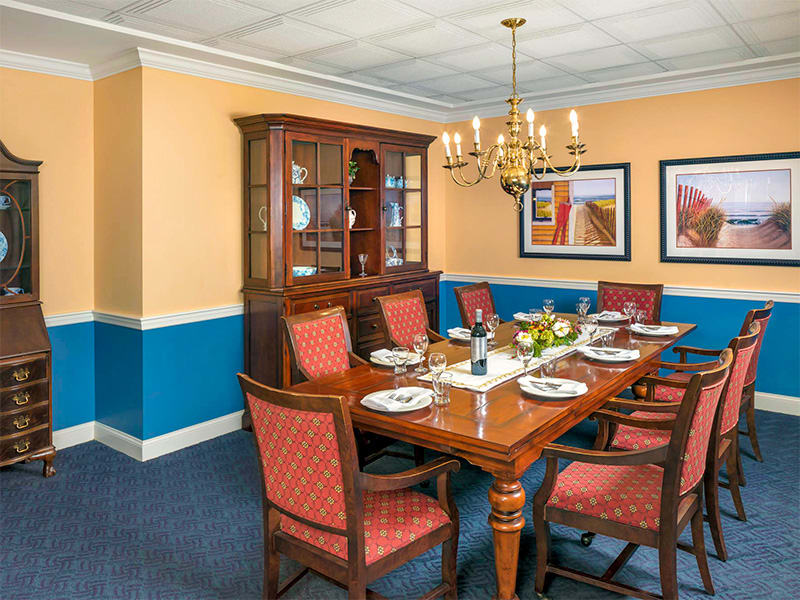 A well-decorated dining room featuring a wooden table set for a meal, surrounded by upholstered chairs and illuminated by a chandelier.