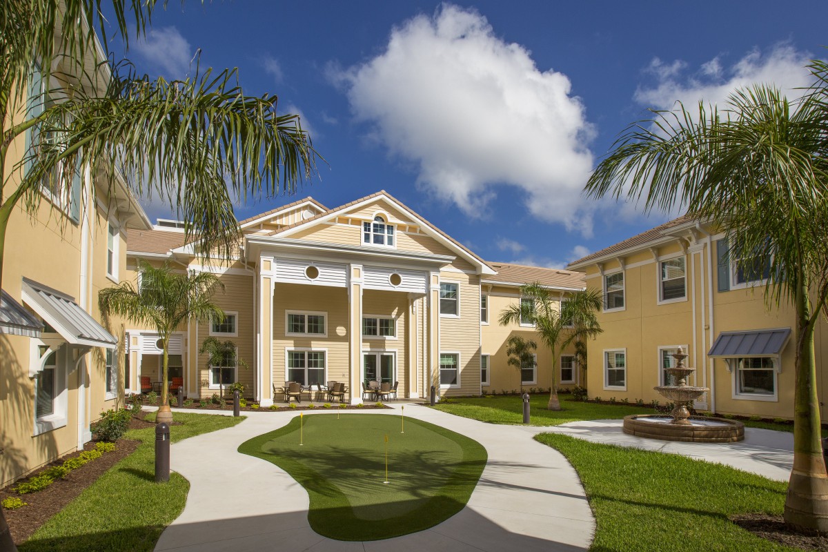 A residential building surrounded by palm trees under a sunny, cloudy sky.