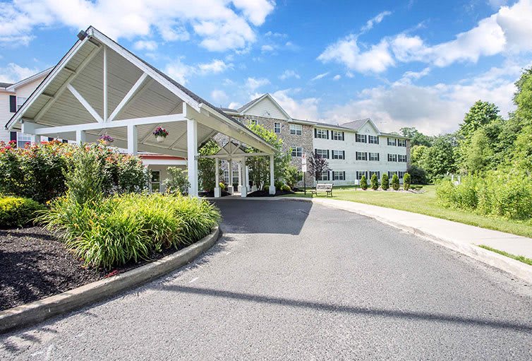 A welcoming entrance of a hotel with a driveway surrounded by lush landscaping under a bright blue sky.