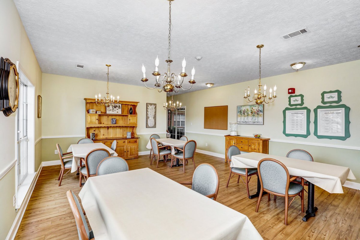 A cozy dining room with chandeliers, tables, and chairs on a wooden floor.
