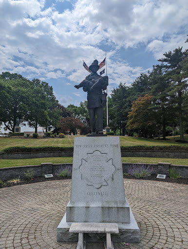 A statue standing prominently in a park, surrounded by greenery and under a partly cloudy sky.