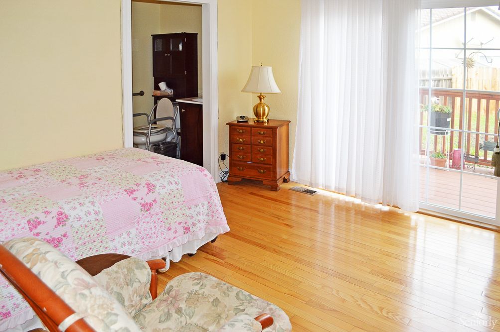 A cozy bedroom with wooden floors, featuring a bed, dresser, and a lamp by the window.