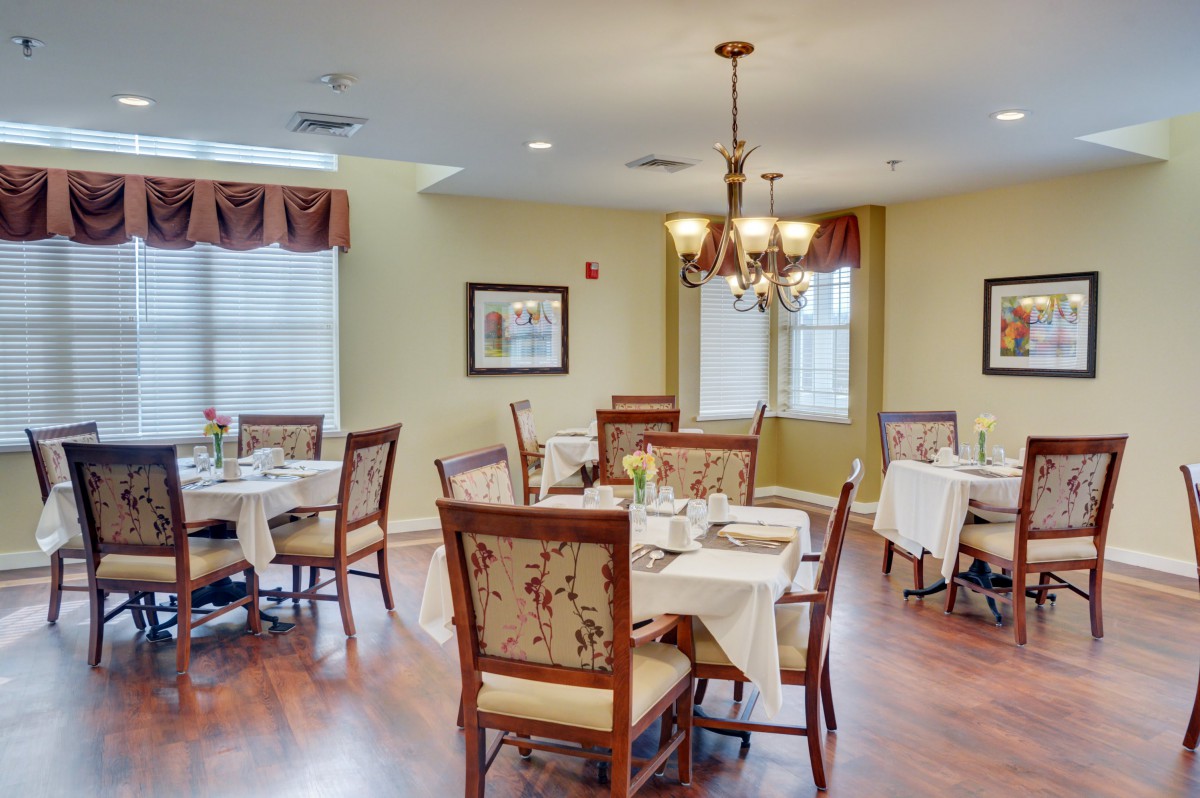 A cozy dining room with neatly arranged tables and chairs under a chandelier.