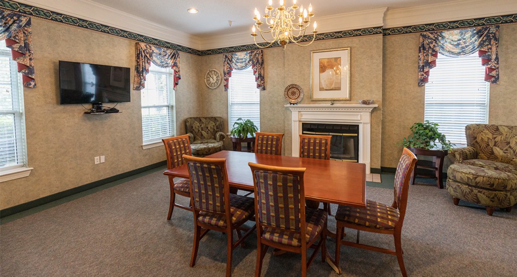 A formal dining room with a wooden table, chairs, and a chandelier above. A fireplace is present along with artwork on the wall.