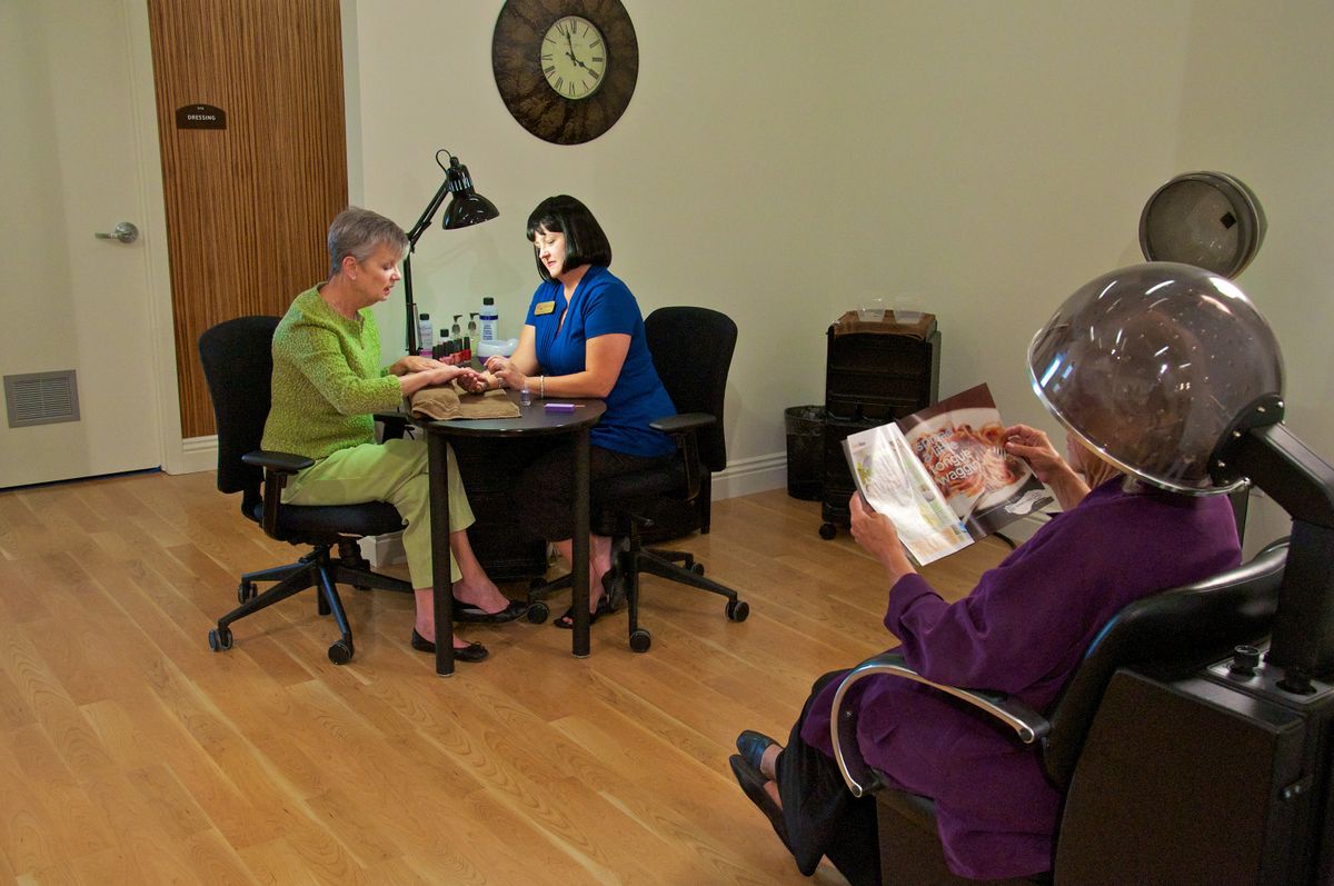 A serene salon where a client receives a manicure while another person waits, reading a magazine.