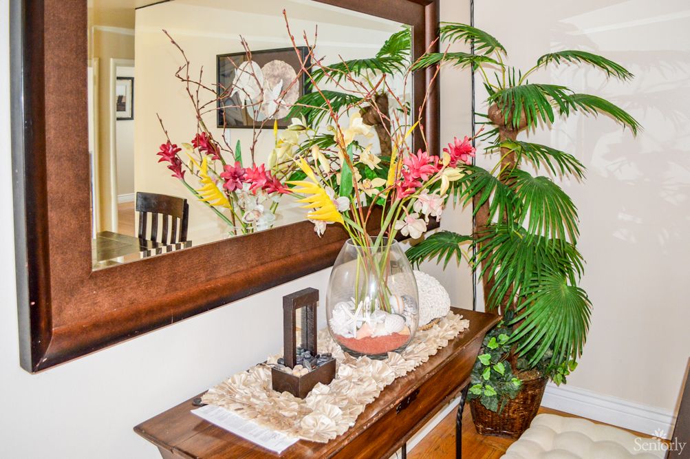 A beautifully decorated interior space featuring a vase with vibrant flowers, a large mirror, and lush green plants.