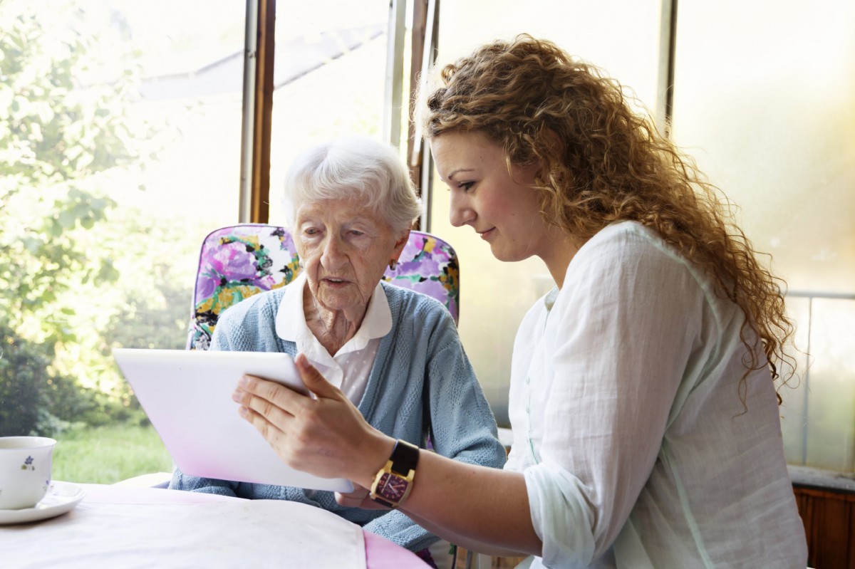 A young woman assisting an elderly woman with a tablet.