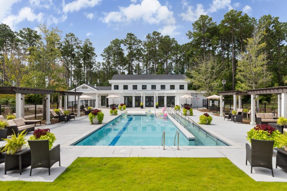 An outdoor swimming pool area with deck chairs and a modern building, surrounded by trees.