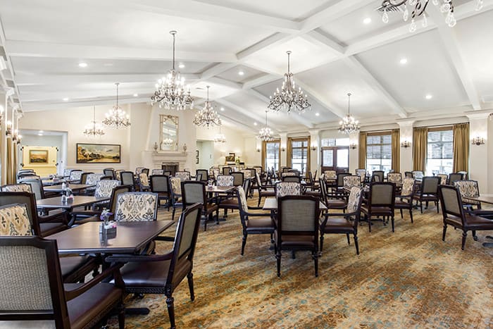 An elegant and spacious dining area with chandeliers, featuring multiple tables and chairs.