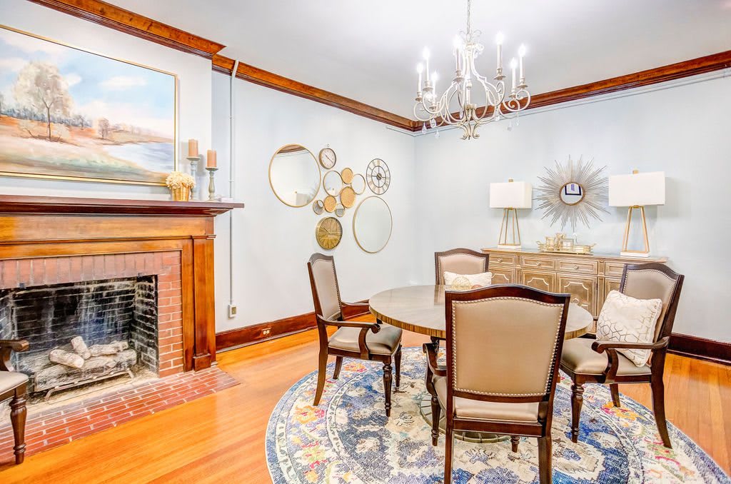 A cozy dining room featuring a round table and chairs, decorated with a chandelier and surrounded by decorative mirrors and a fireplace.