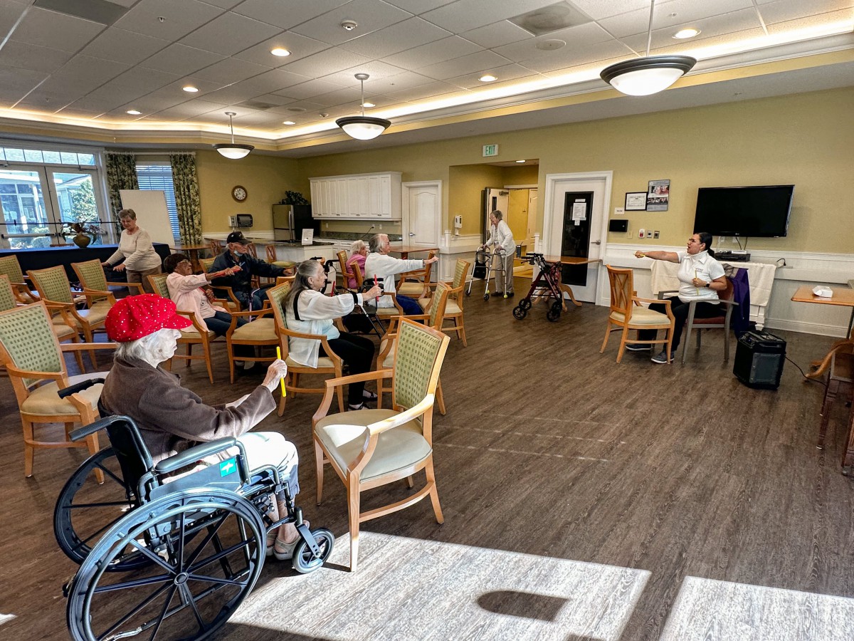 A group of seniors gathered in a nursing home's common area, engaging in various activities.