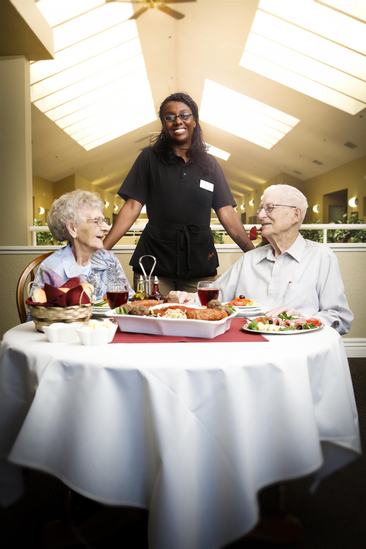 Elderly couple enjoying a meal at a restaurant with a cheerful server.