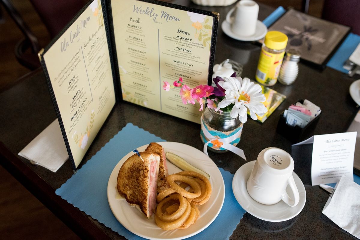 A table setting at a restaurant with a sandwich and onion rings, accompanied by coffee and a menu.