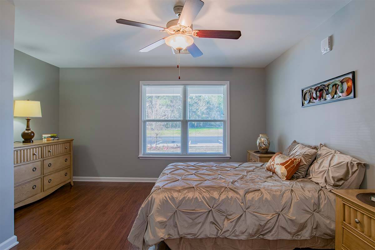A cozy bedroom with a large bed, ceiling fan, and window allowing natural light to fill the room.