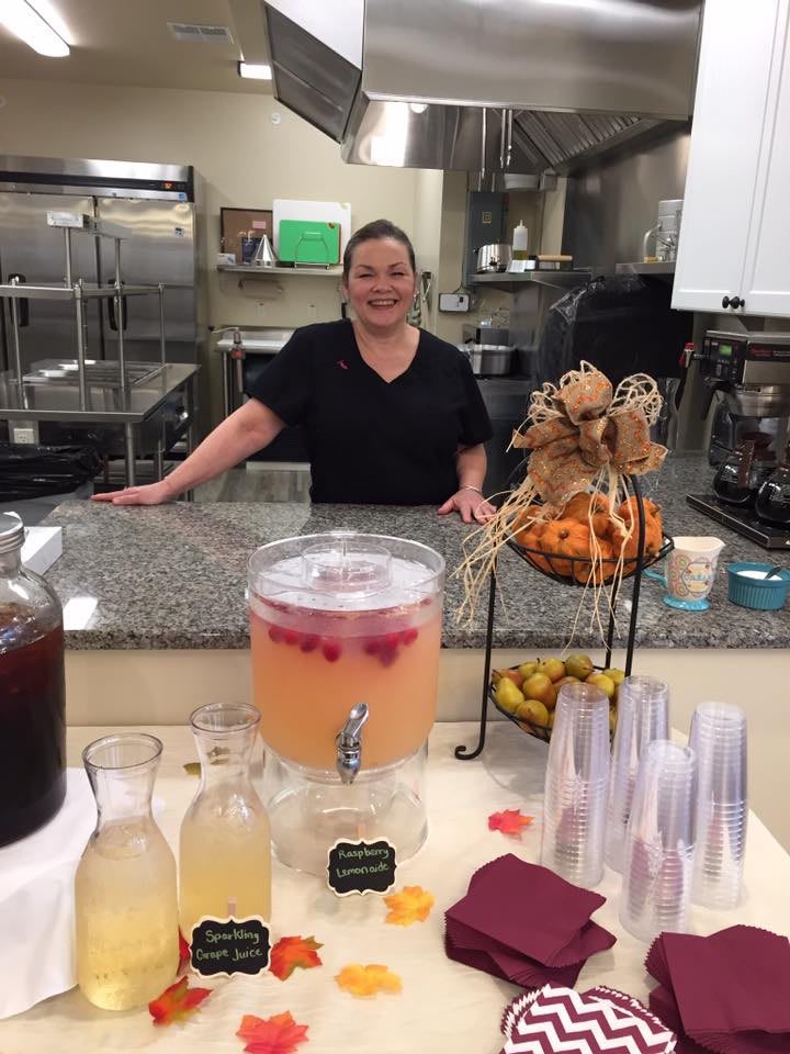 A person standing behind a kitchen counter with beverages and snacks displayed.