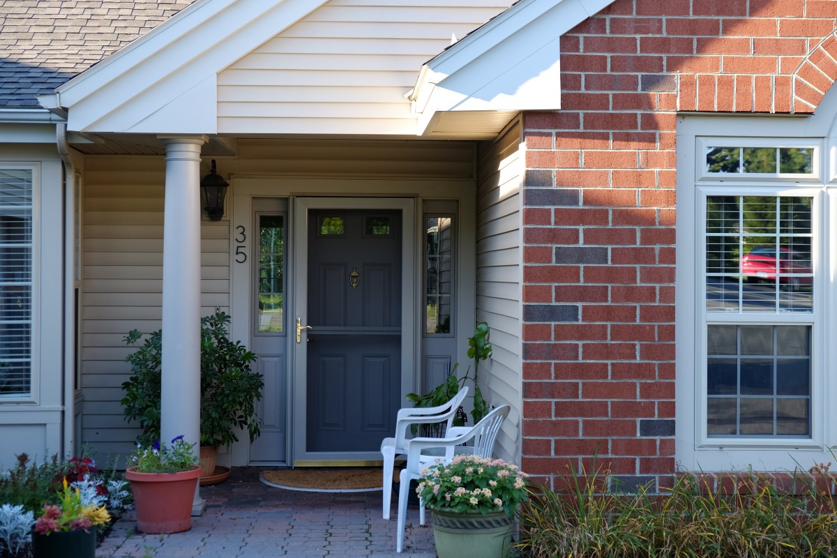 A cozy front porch with a blue door, white chairs, and potted plants.
