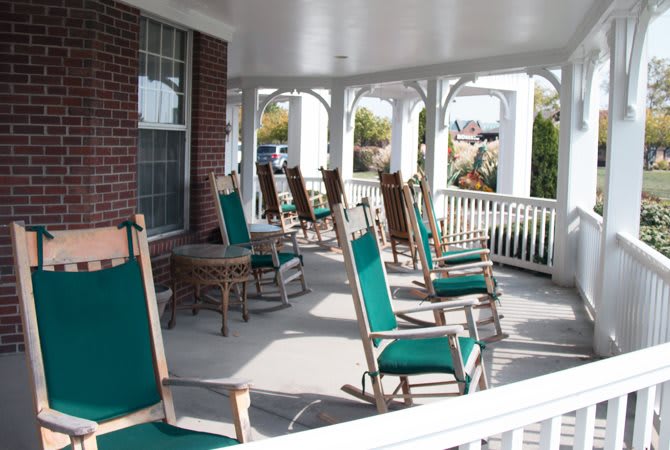 A covered porch with several rocking chairs arranged in a row.