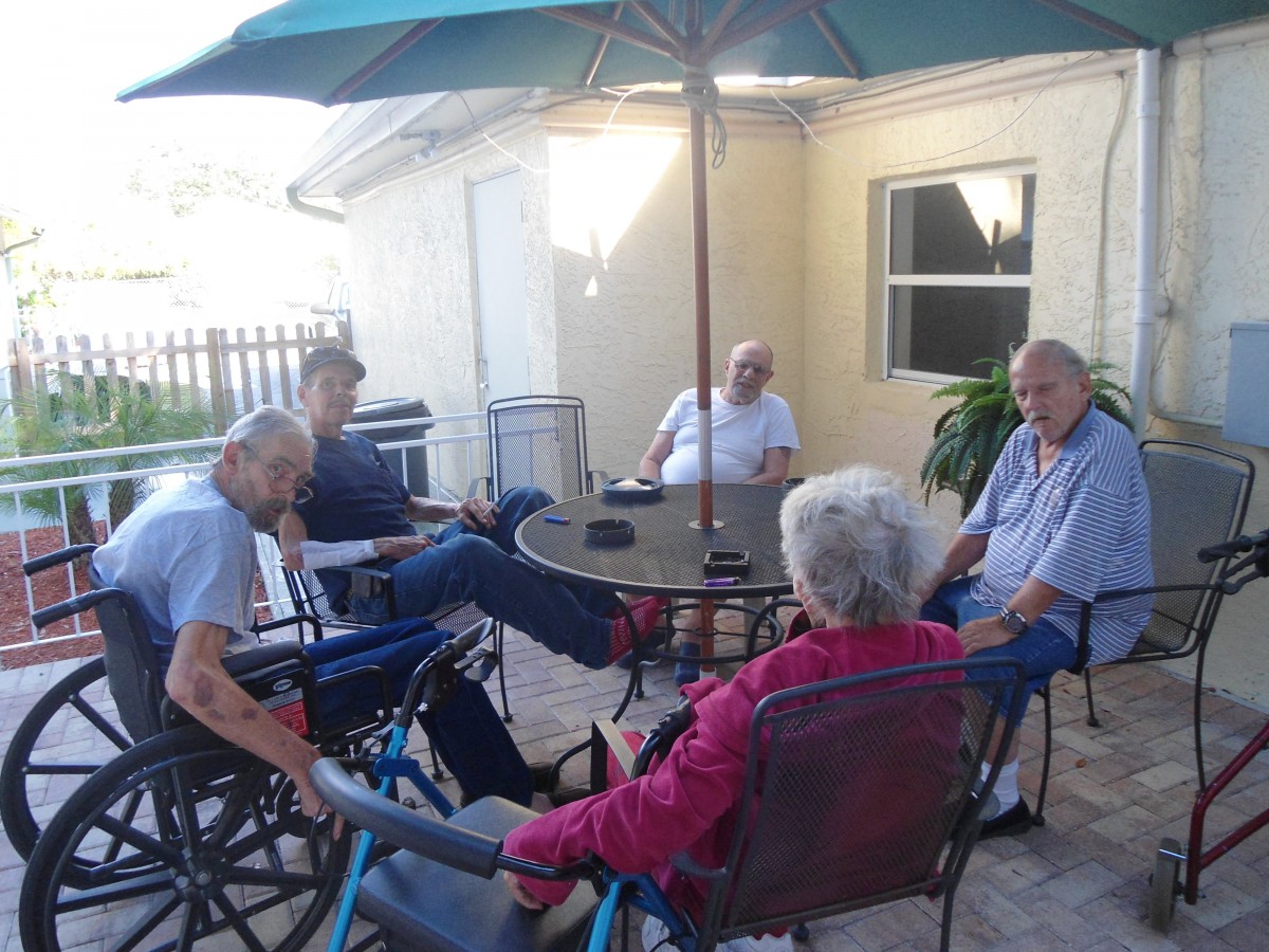 A group of people sitting and socializing on a patio under an umbrella.
