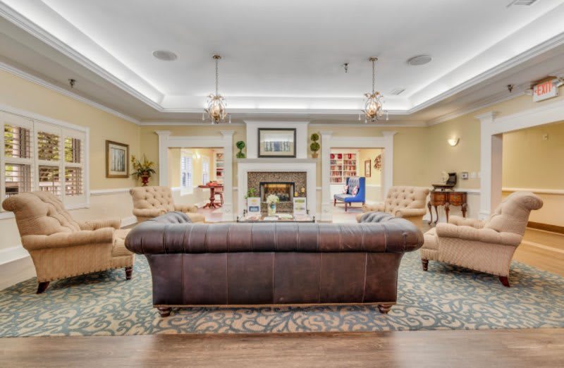 A tastefully decorated traditional living room featuring a central leather sofa, flanked by armchairs, with elegant chandeliers and a fireplace focal point.