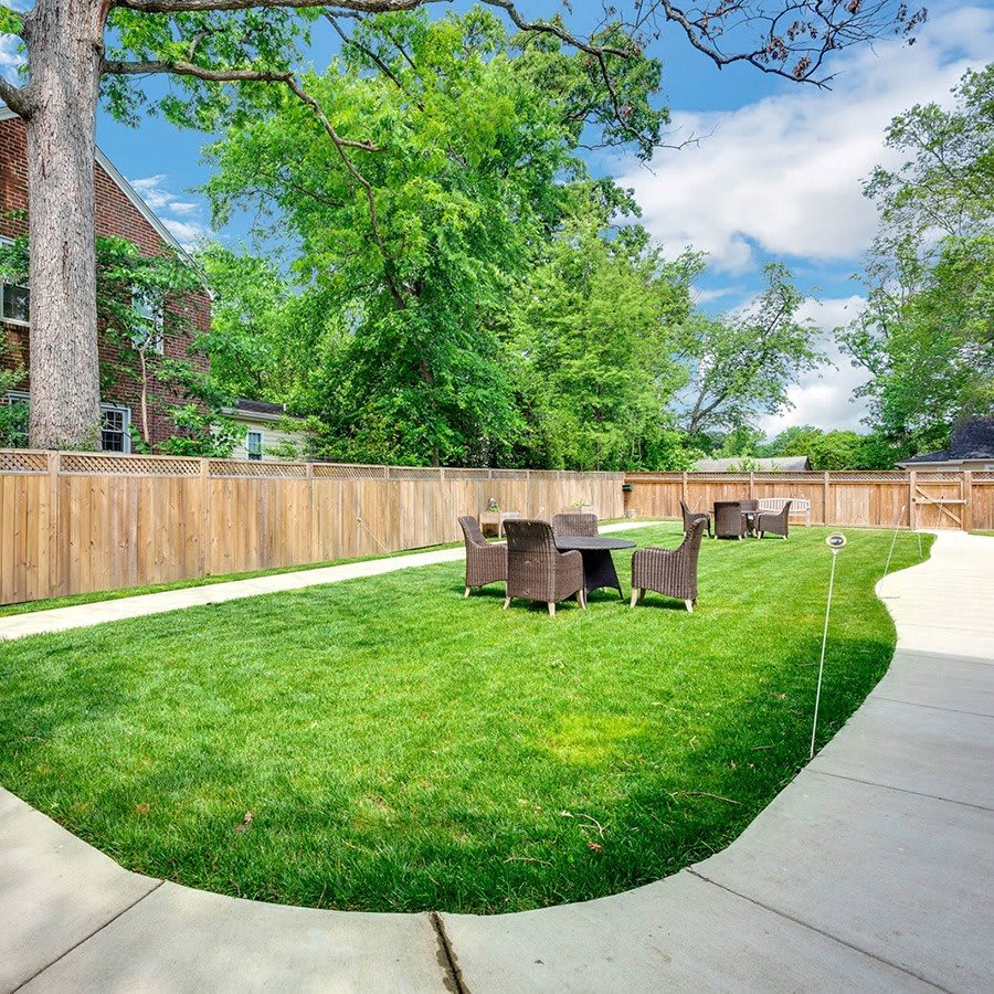 A spacious backyard with outdoor furniture set on a well-maintained lawn, surrounded by tall trees and a wooden fence.