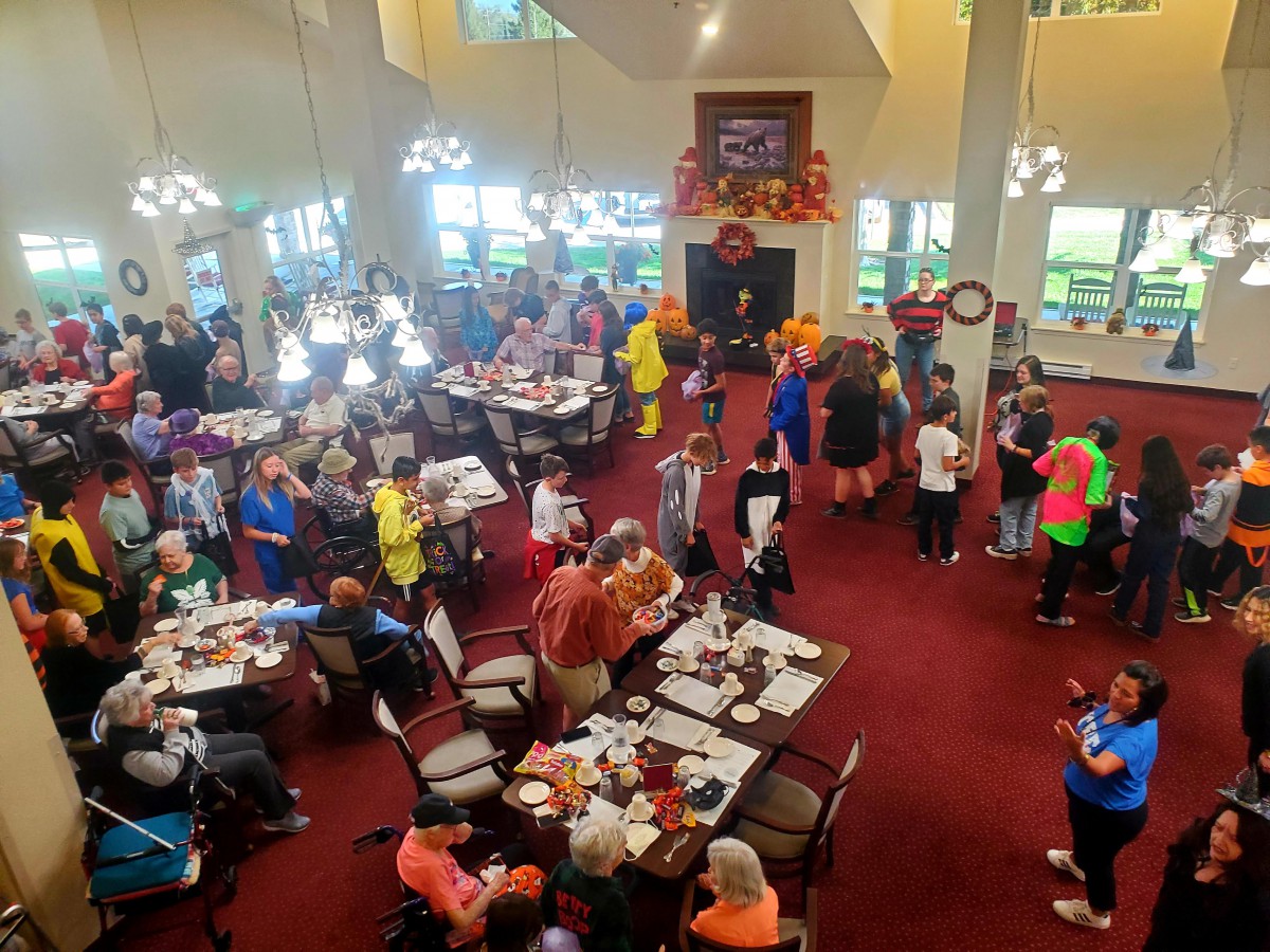 A large group of people gathered indoors for a community event, with tables set for dining.