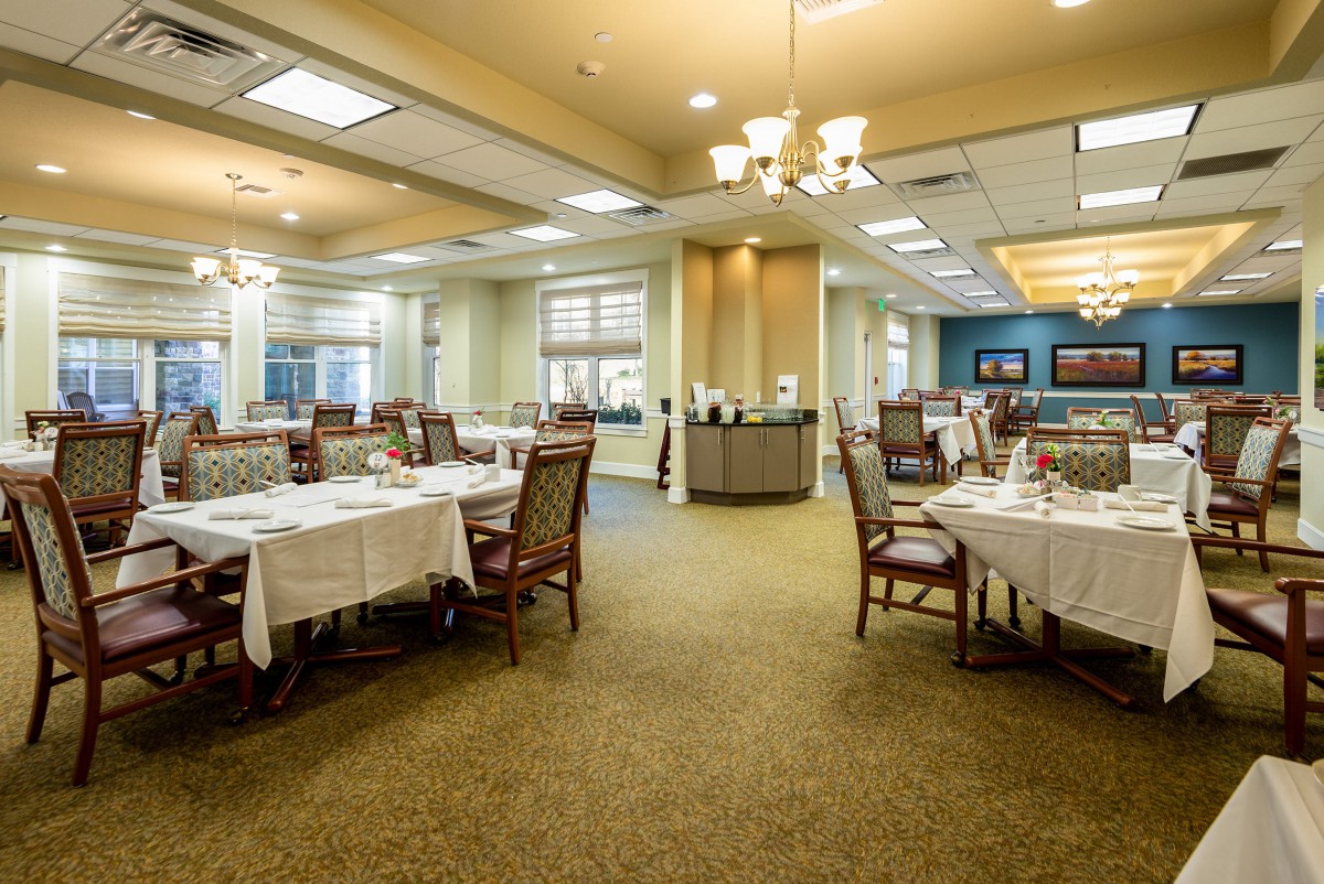 An elegant dining room with neatly arranged tables and chairs, illuminated by chandeliers.