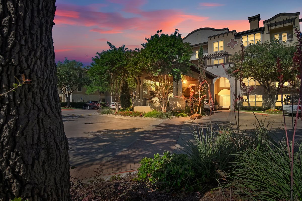 A picturesque view of a building at sunset, with warm lights and surrounding trees.