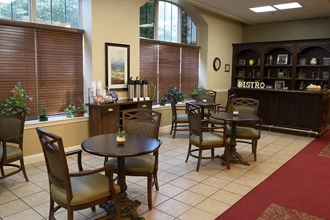 Cozy cafe interior with tables, chairs, and a coffee station near large windows.