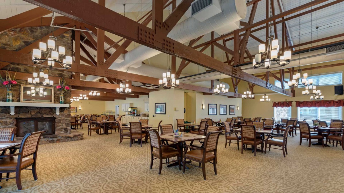 A spacious restaurant dining area with elegant chandeliers and wooden beams.