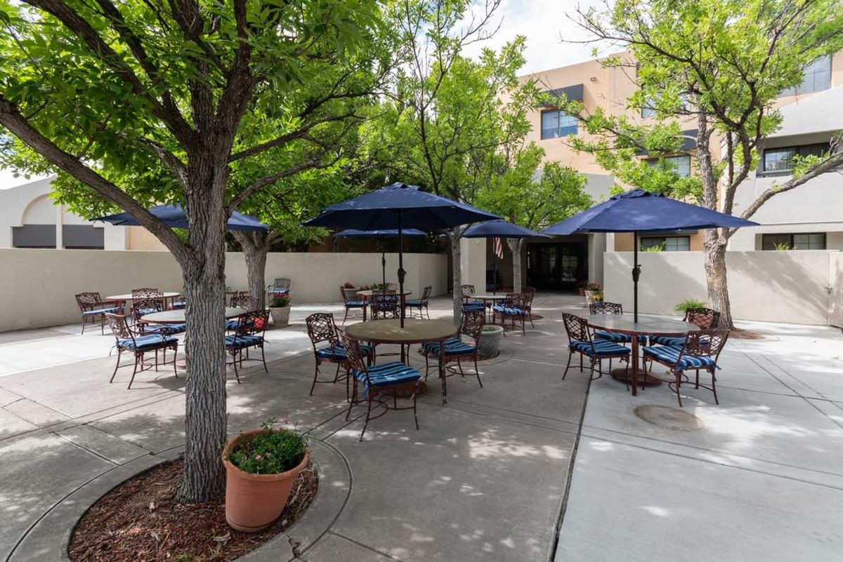 A peaceful patio area with outdoor seating, featuring tables and chairs under blue umbrellas surrounded by greenery.