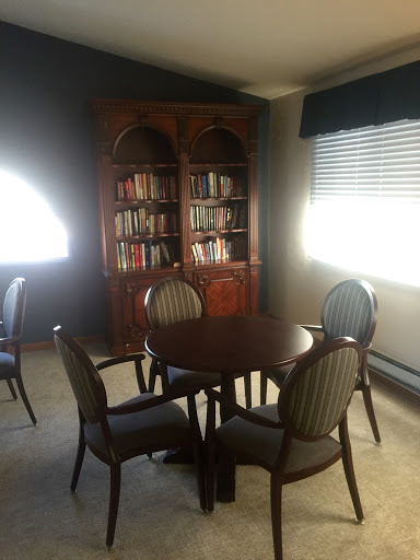 A cozy reading nook featuring a round table surrounded by upholstered chairs and a wooden bookshelf filled with books.