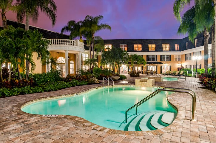 A luxurious resort with a beautifully lit swimming pool surrounded by palm trees at dusk.