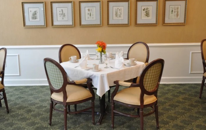 A neatly set dining table with four chairs, featuring a white tablecloth and decorative artwork on the walls.