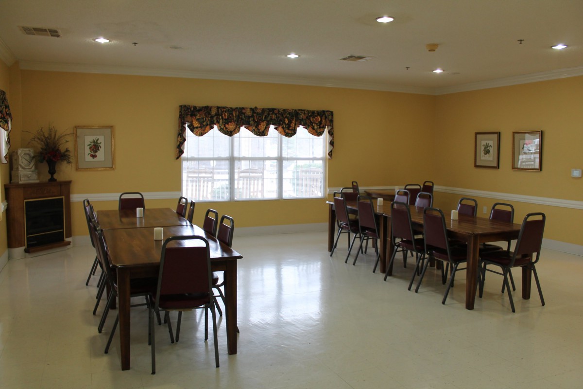 An empty dining room with wooden tables and chairs, featuring a large window with curtains.