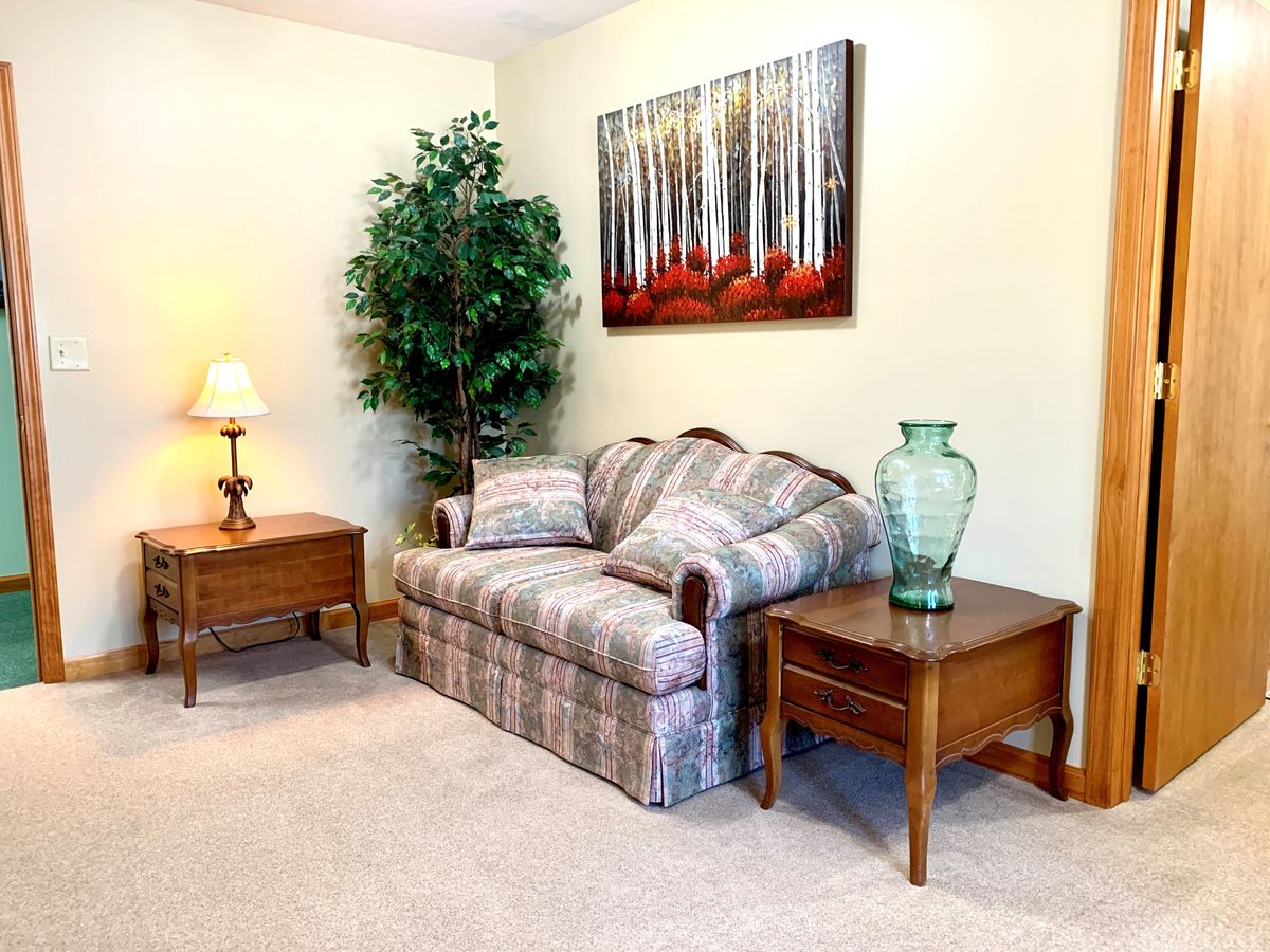 A cozy living room with a plaid sofa, side tables, and decorative elements like a lamp, indoor plant, wall art, and a vase.