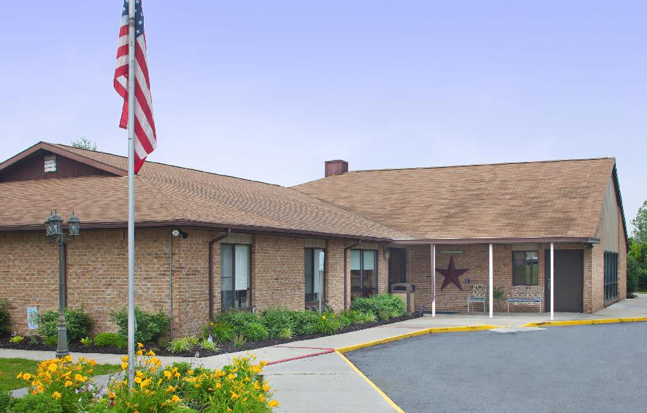 A single-story brick building with an American flag in the foreground and landscaped greenery.