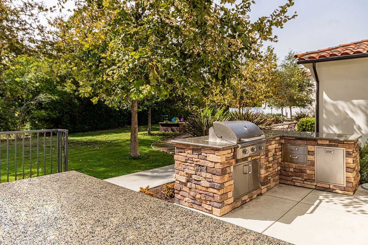 A well-maintained backyard featuring a stone barbecue grill and lush greenery.