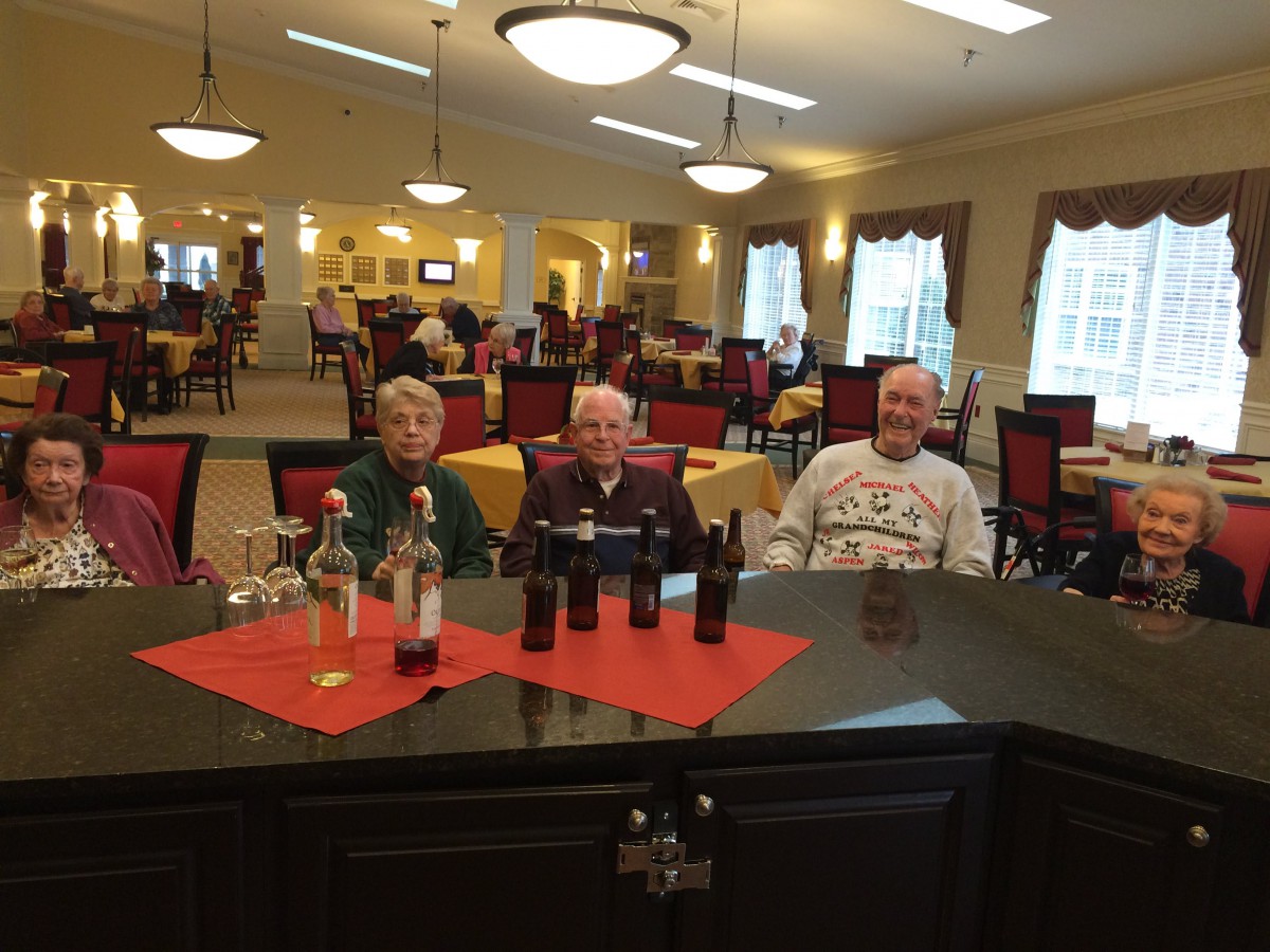 A group of elderly people seated at a table in a restaurant, with bottles on the table.