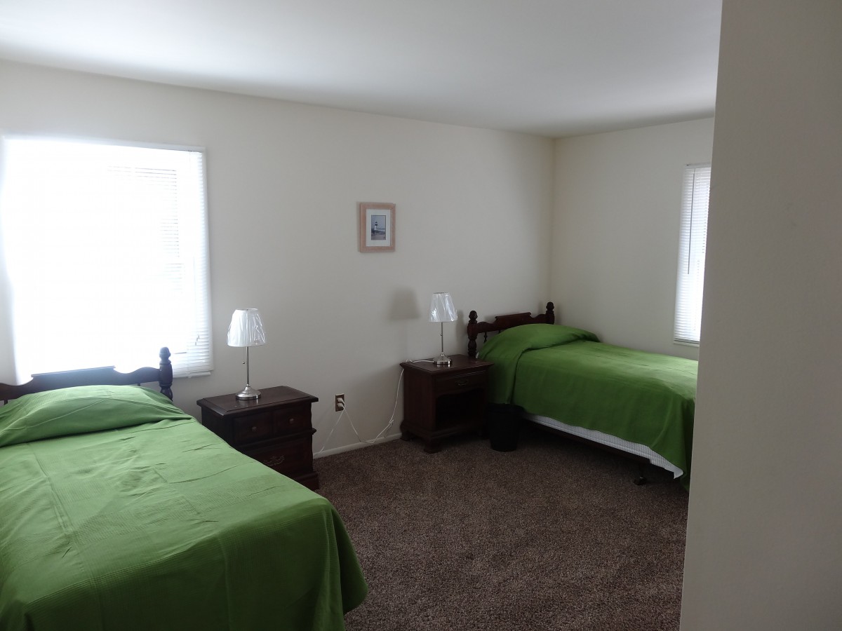 A simple bedroom with two twin beds featuring green bedding, furnished with nightstands and lamps.