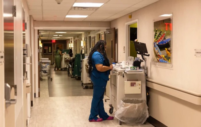 A nurse in blue scrubs works at a medical station in a hospital corridor.