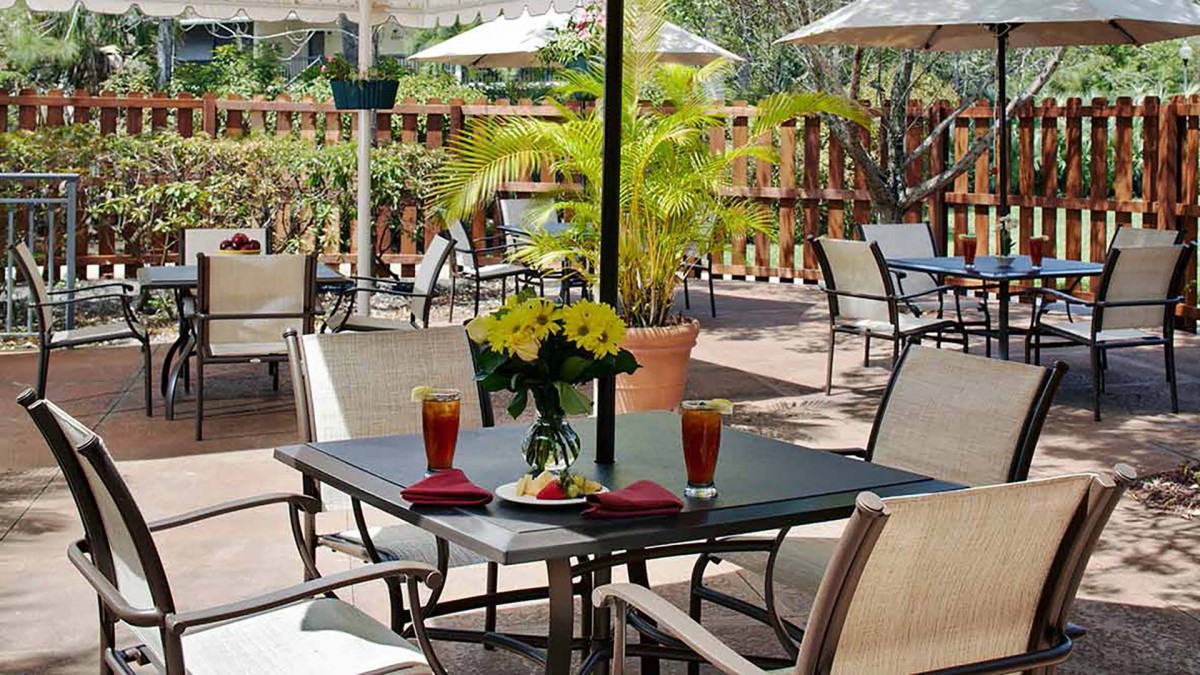An inviting outdoor seating area with a table set for two, featuring flowers and drinks under the shade of umbrellas.