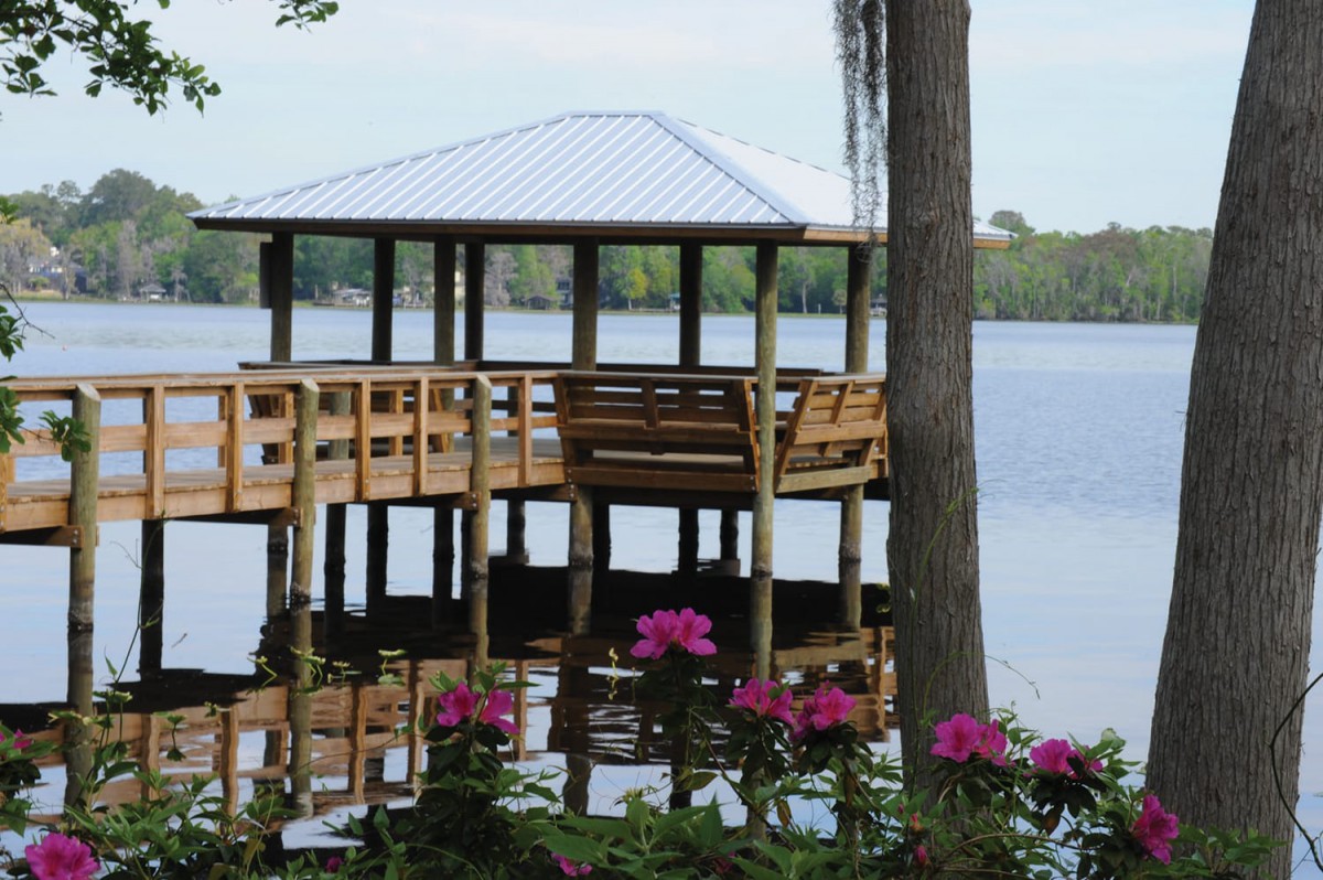 A wooden gazebo by the lake with blooming flowers in the foreground.
